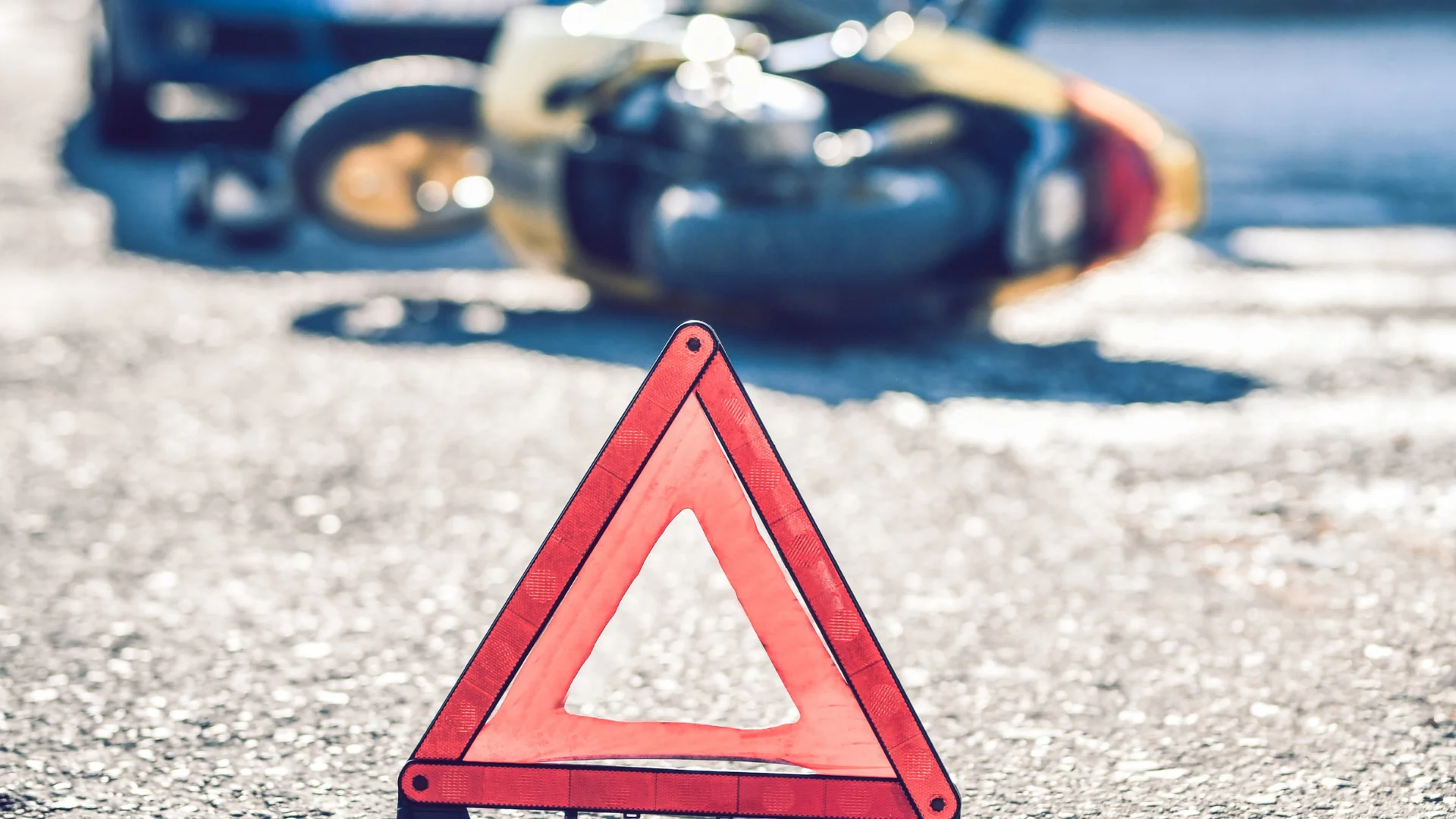 a roadside caution marker with a yellow motorcycle in the background that's been hit by a car 