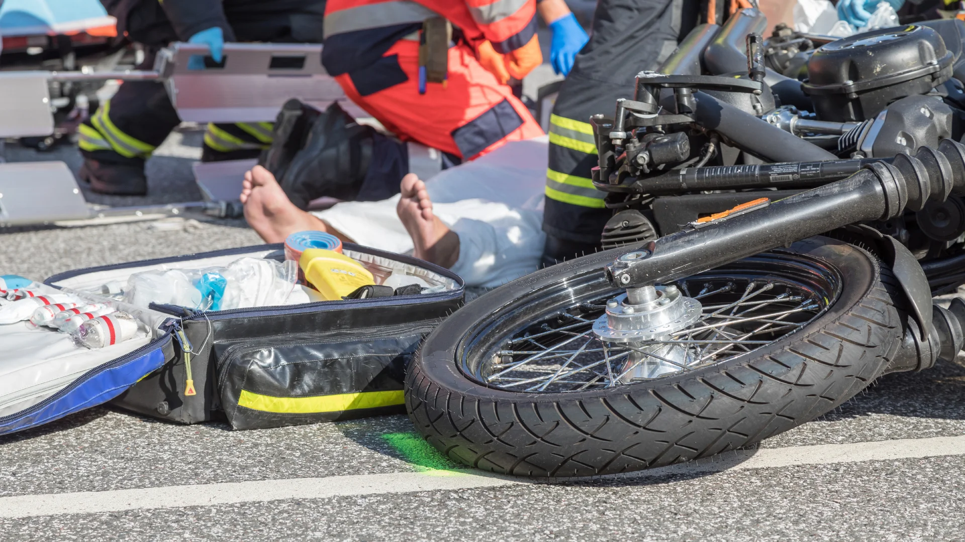 the aftermath of a motorcycle crash, with the rider on the ground being worked on by first responders
