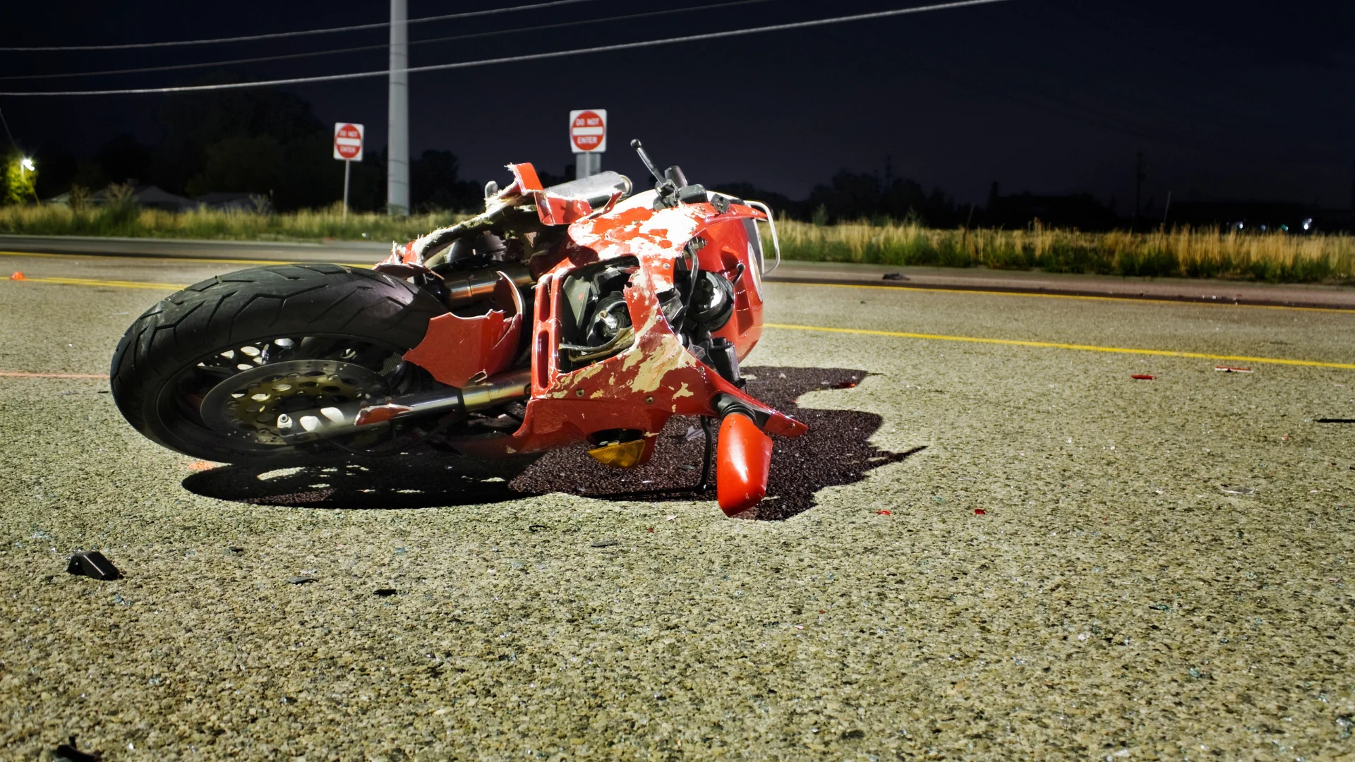 a red motorcycle laying on its side on a highway after an accident with Do Not Enter street signs in the background
