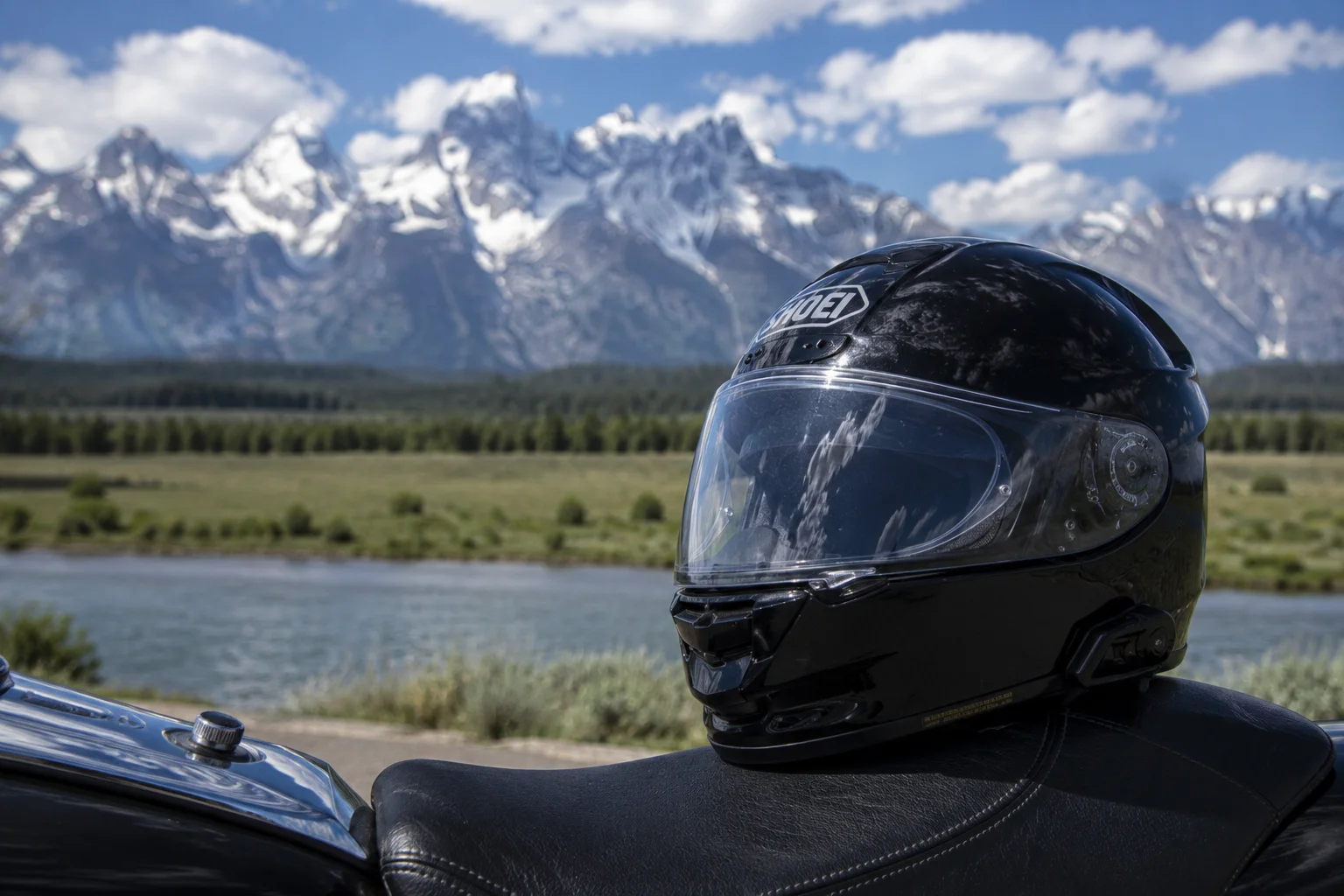 A black motorcycle helmet resting on the seat of a motorcycle with the Grand Tetons in the background