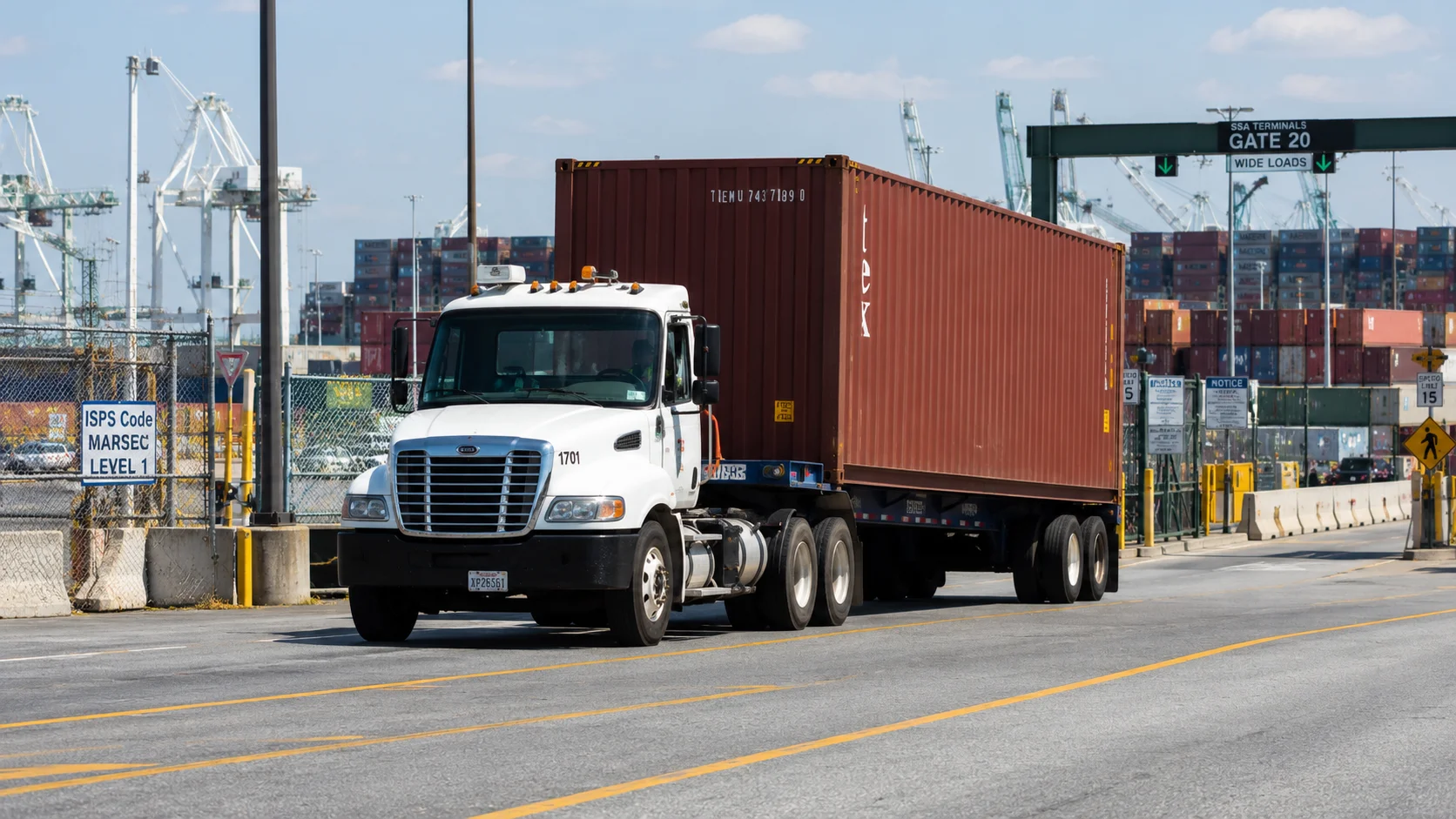 Drayage truck hauling a sealed shipping container on a chassis leaving a Port of Seattle marine terminal