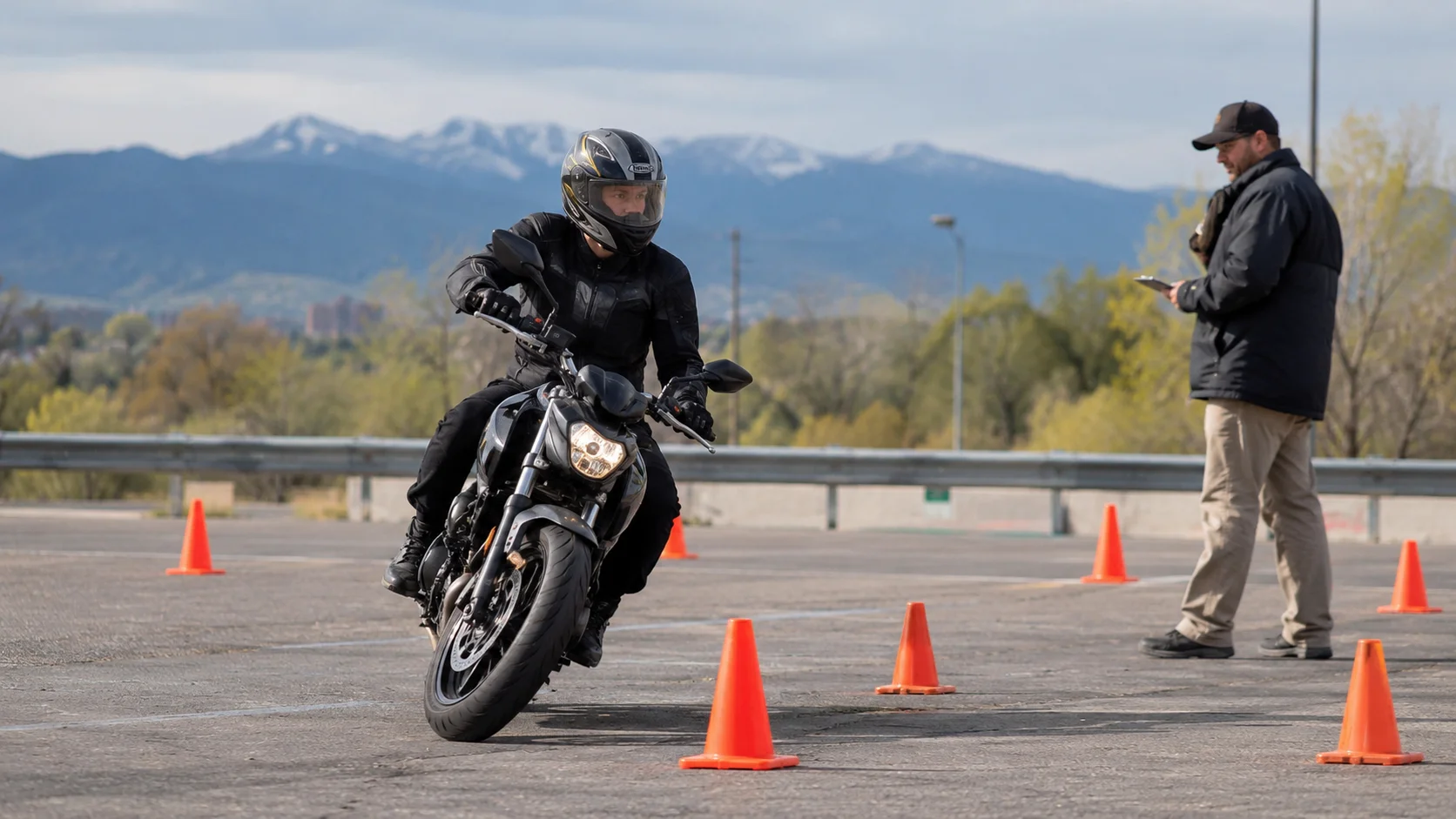 Helmeted rider navigating a motorcycle skills test course in Colorado as an examiner watches with a clipboard.