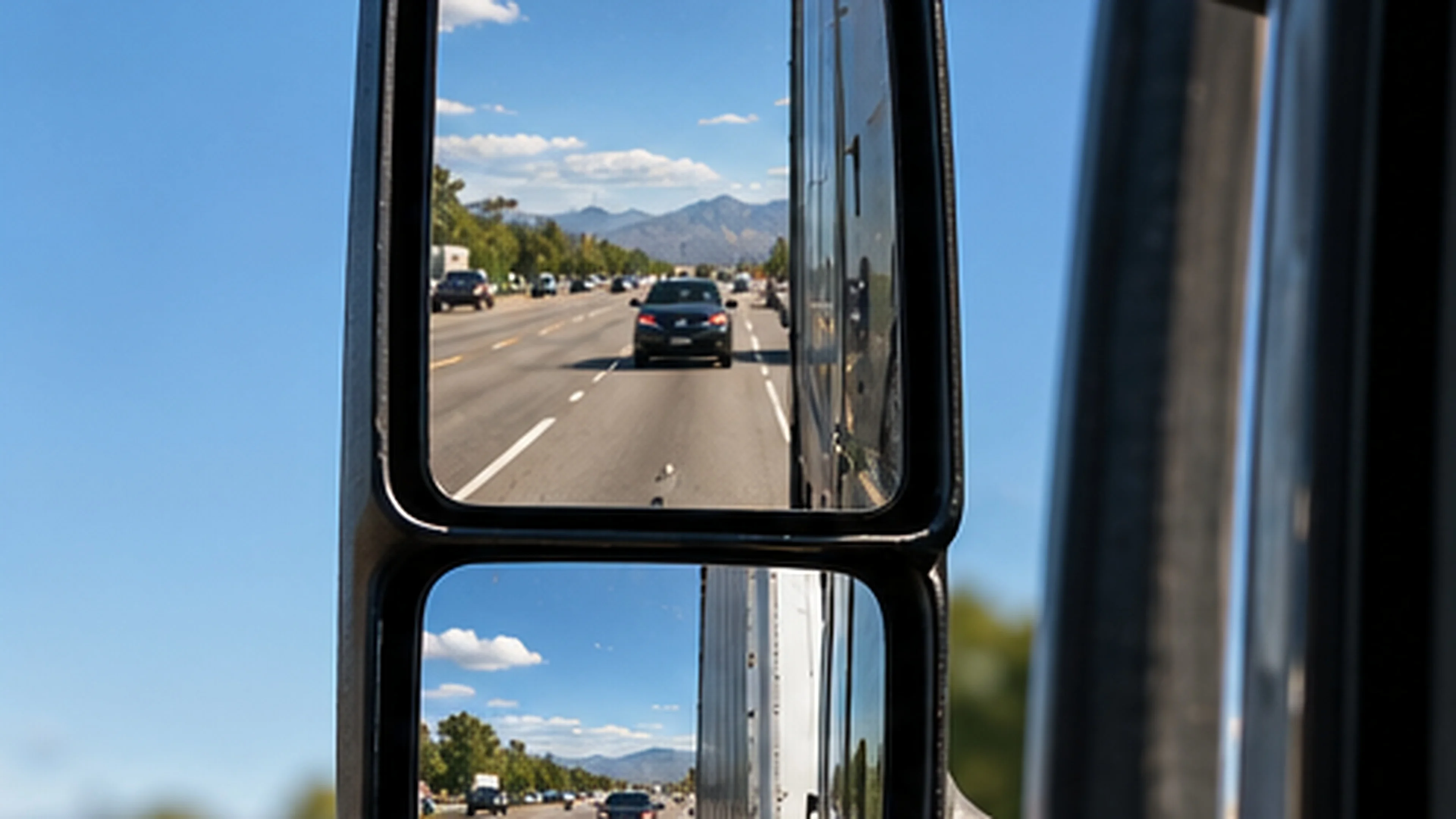 Passenger car visible in a semi-truck's side mirror, highlighting commercial truck blind spots and the importance of checking mirrors before changing lanes.