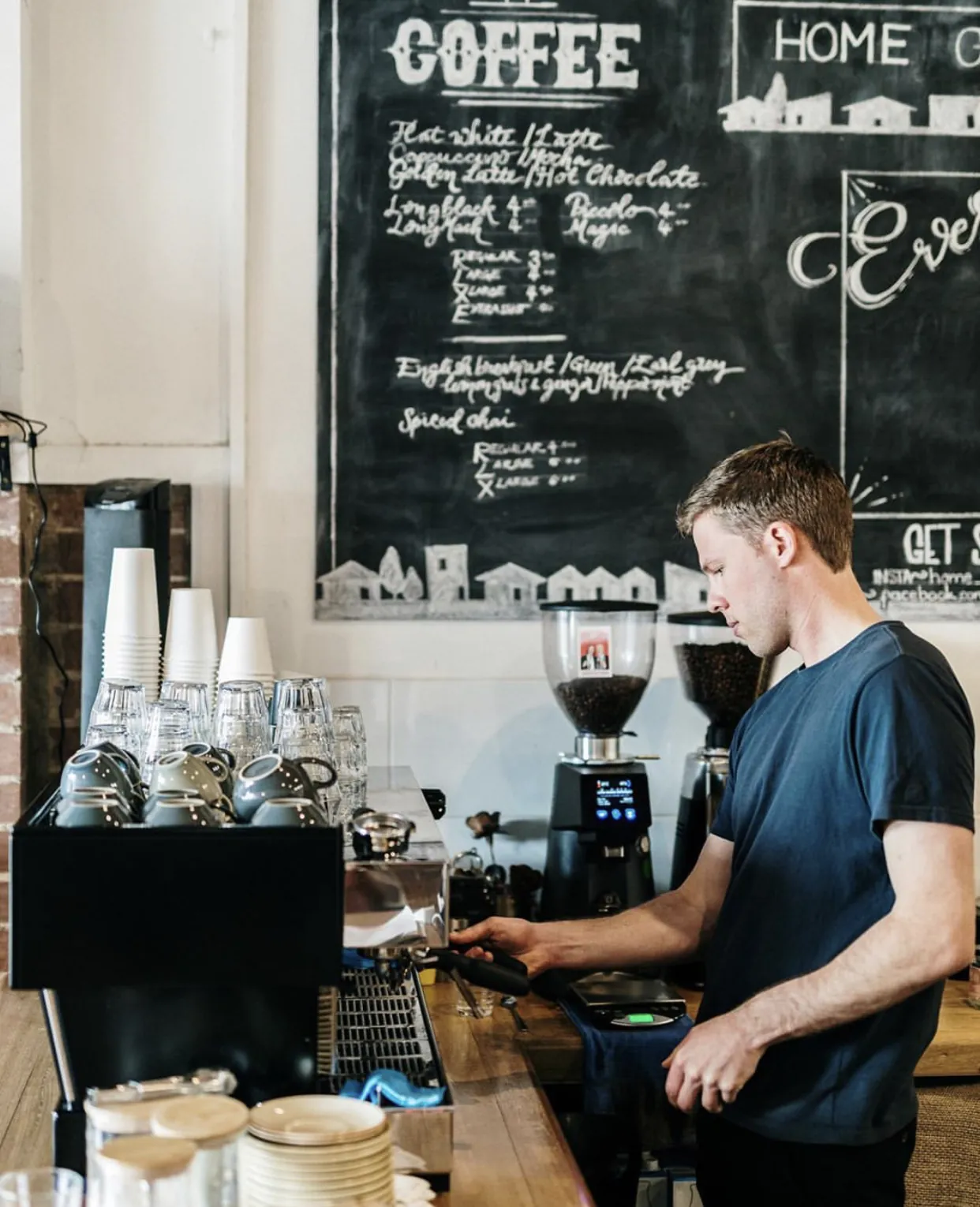 Barista in front of the chalkboard menu at HomeGround Café