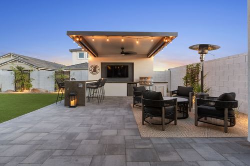 An image of a completed project in Scottsdale, AZ that features an aluminum pergola, television wall and a outdoor kitchen. The foreground shows a seating area and installation of concrete pavers.