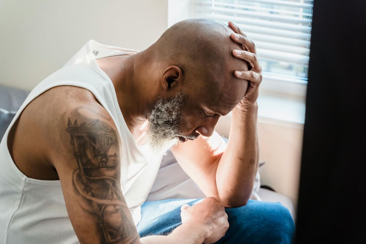homme désemparé assis sur son lit, la main sur la tête