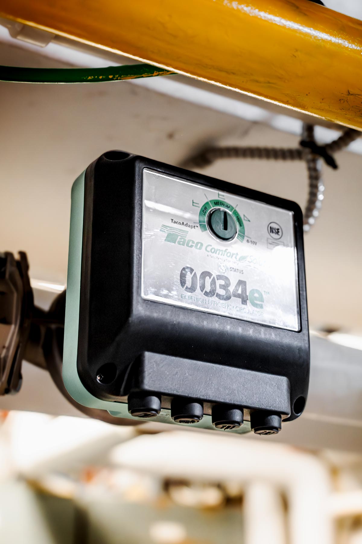 Close-up of a Taco Comfort Solutions 0034e high-efficiency circulator pump with a black and green control box mounted on plumbing pipes.