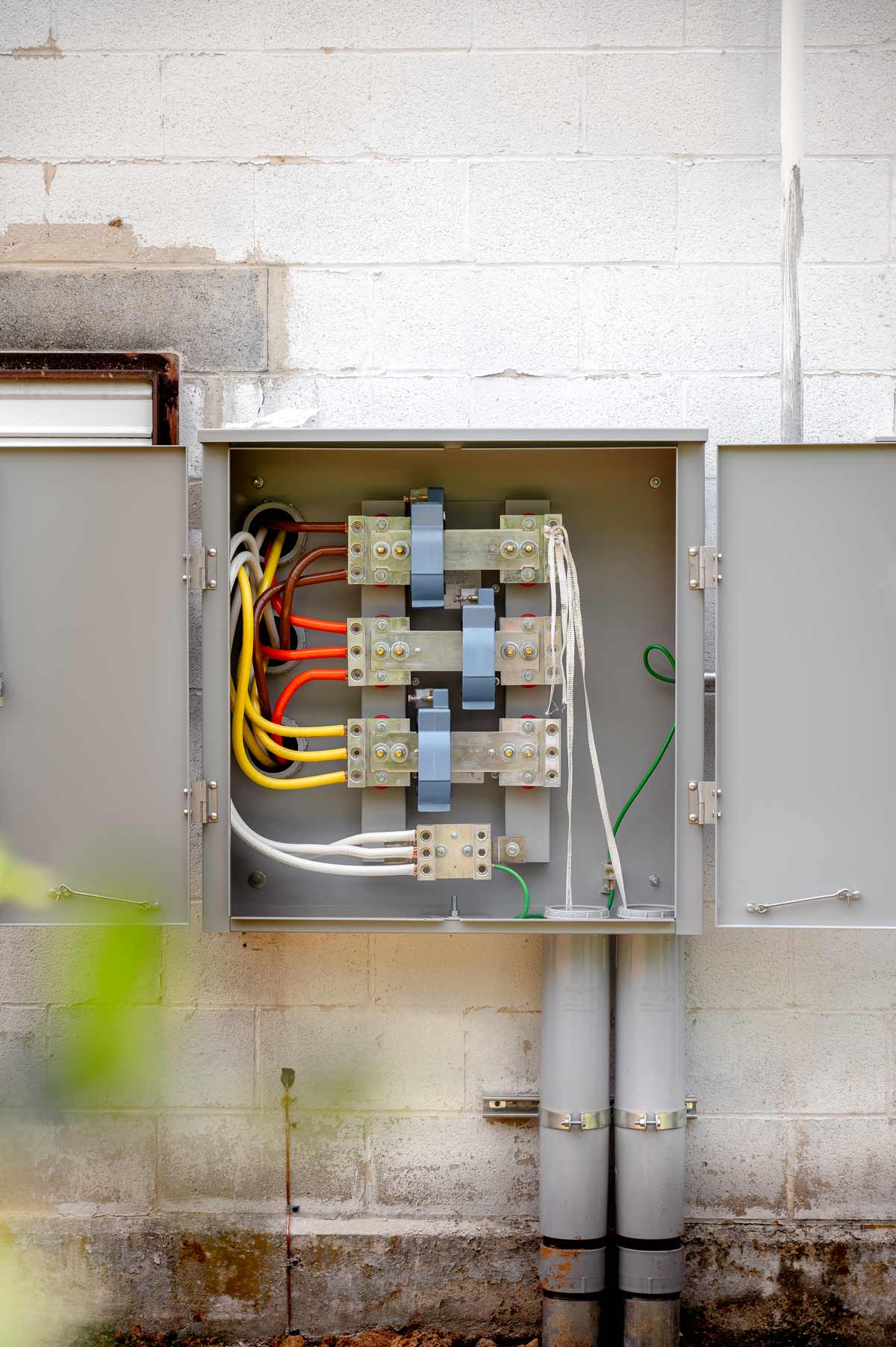 Open electrical utility box mounted on a weathered white brick wall with colored cables and metal connectors inside.