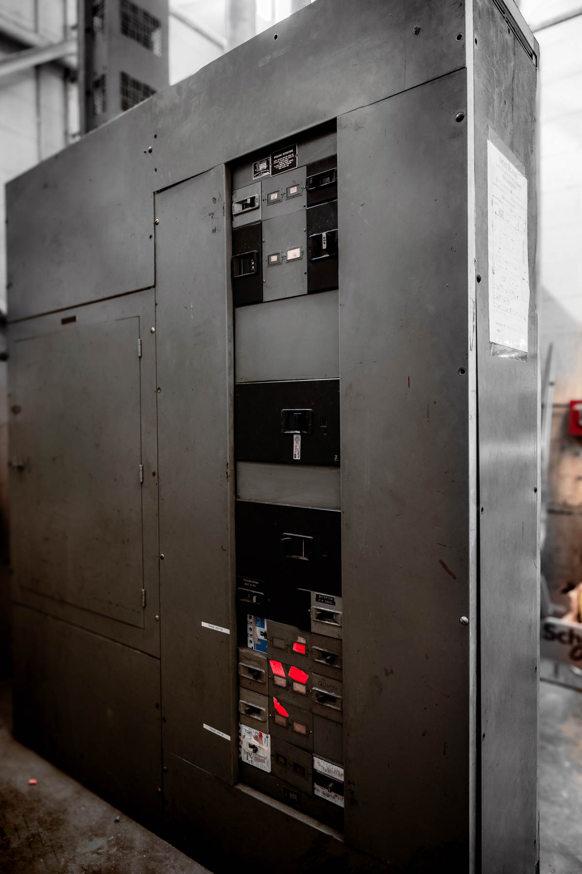 Large industrial electrical control panel with multiple switches and circuit breakers in a warehouse setting.