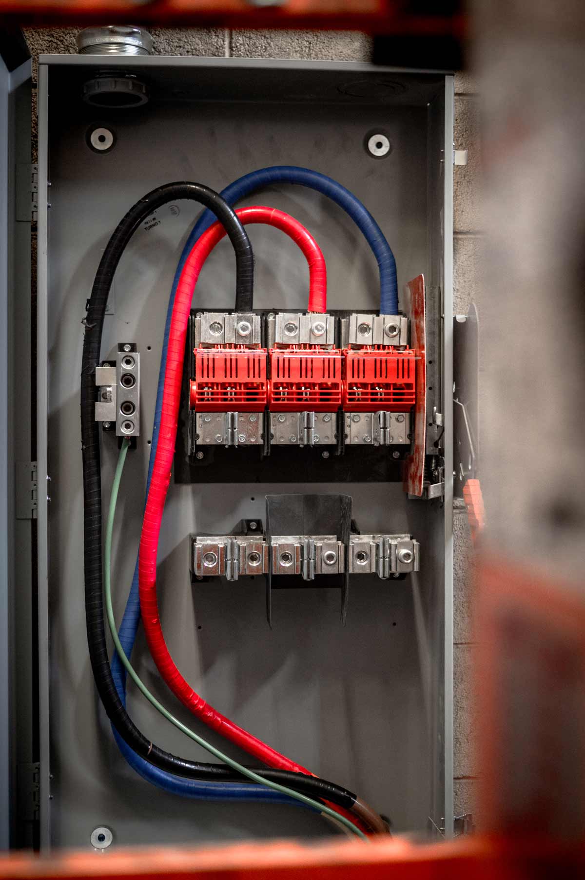 Electrical panel box with red, blue, black, and green insulated wires connected to circuit terminals.