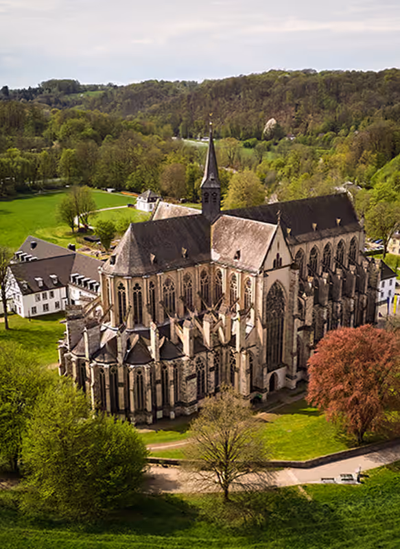 Aerial view of Haus Altenberg with focus on Altenberg Cathedral, framed by green spaces and a natural landscape backdrop