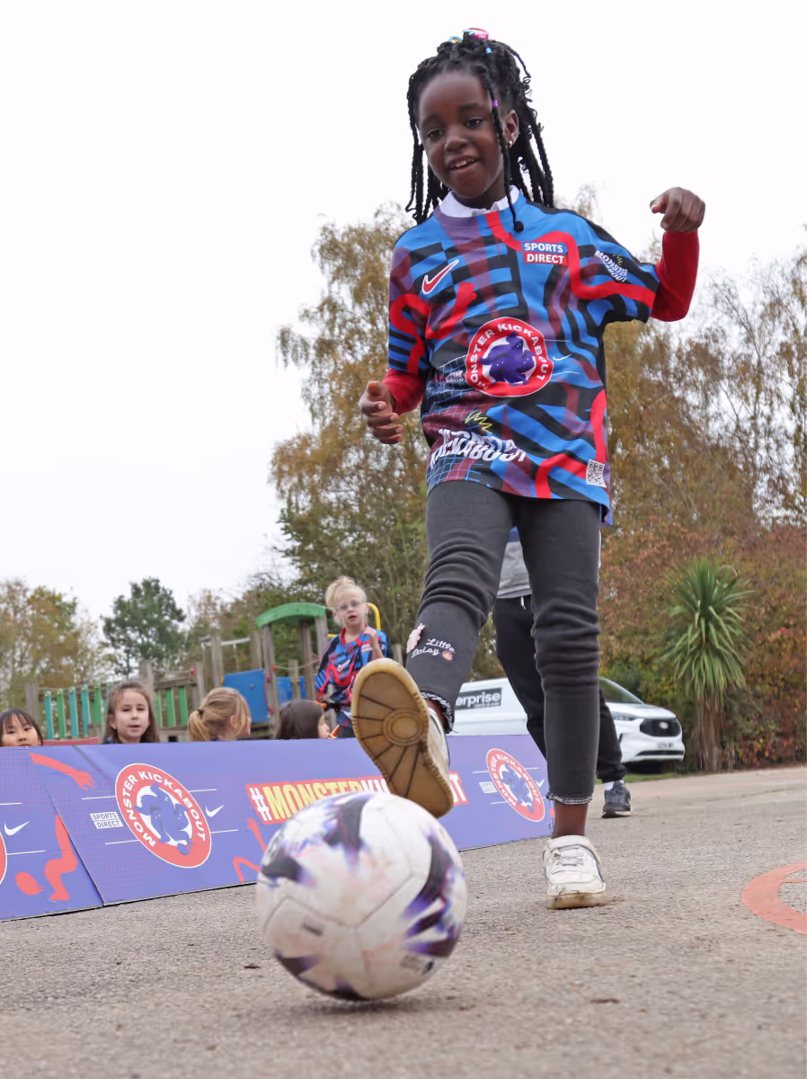 A photograph of a girl playing football wearing little monsters football kit
