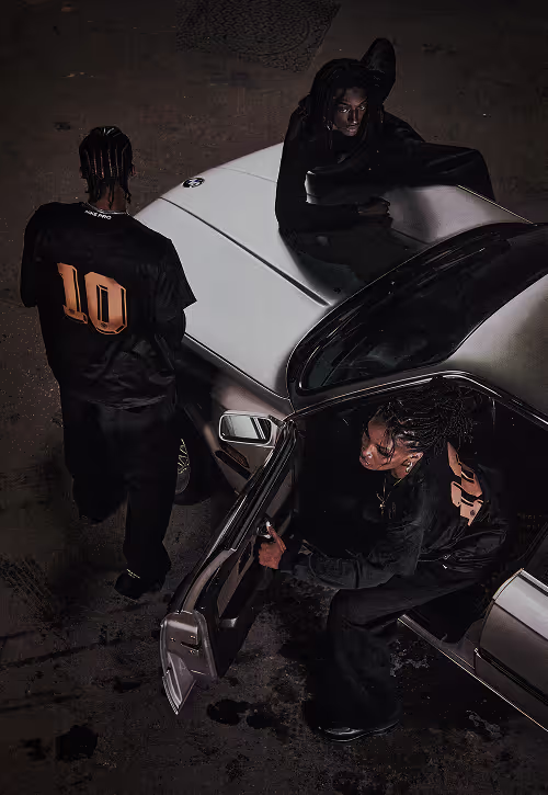 A group of young people wearing BAARA clothing next to a silver BMW