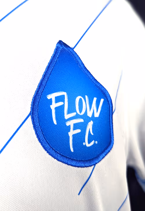 A close-up shot of a football t-shirt with blue stripes and a water droplet shaped emblem with words Flow FC written on it