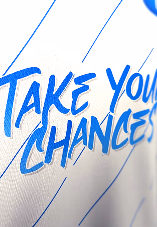 A close-up of a white football t-shirt with thin blue stripes and letters reading Take Your Chance