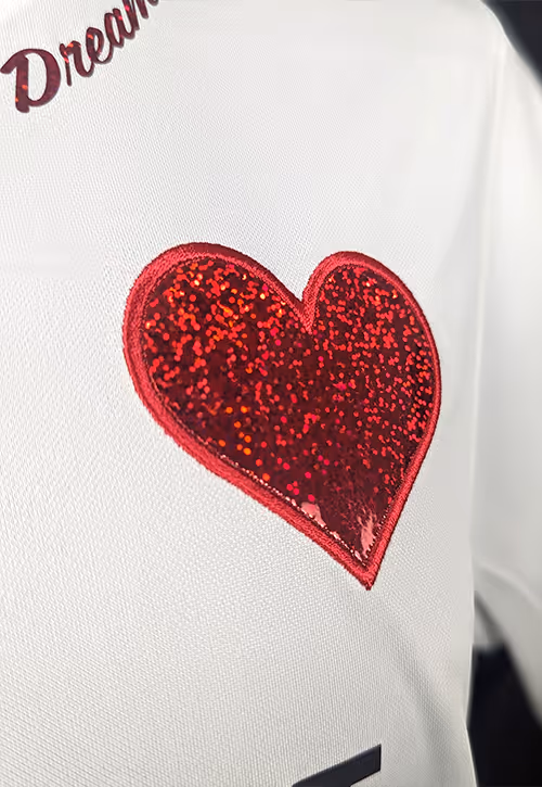 A close-up shot of a football t-shirt with a red heart made of glitter and text "Dream" next to the shoulder.