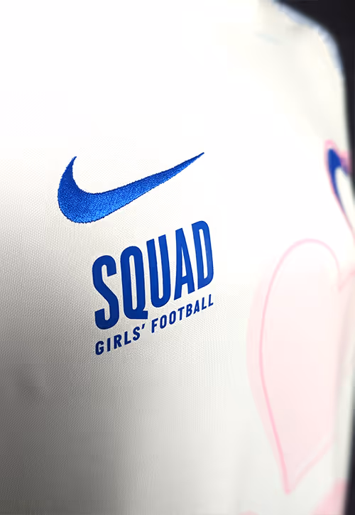 A close-up of a white football t-shirt with a blue Nike swoosh logo, words SQUAD in capitals and Girl's Football underneath. 