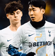 Tottenham Hotspur players warming up in white and navy kits with a gold serpent design; the player in front wears gloves and a neck warmer, with light rain falling around them.