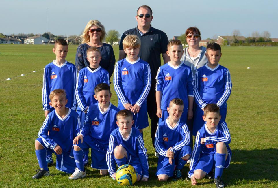 Young boys football team all wearing blue uniform together with their coach