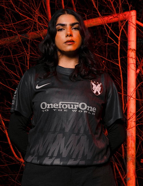 Female standing in front of the football goal wearing black tshirt with NIKE swoosh logo and text reading OneFourOne To The World