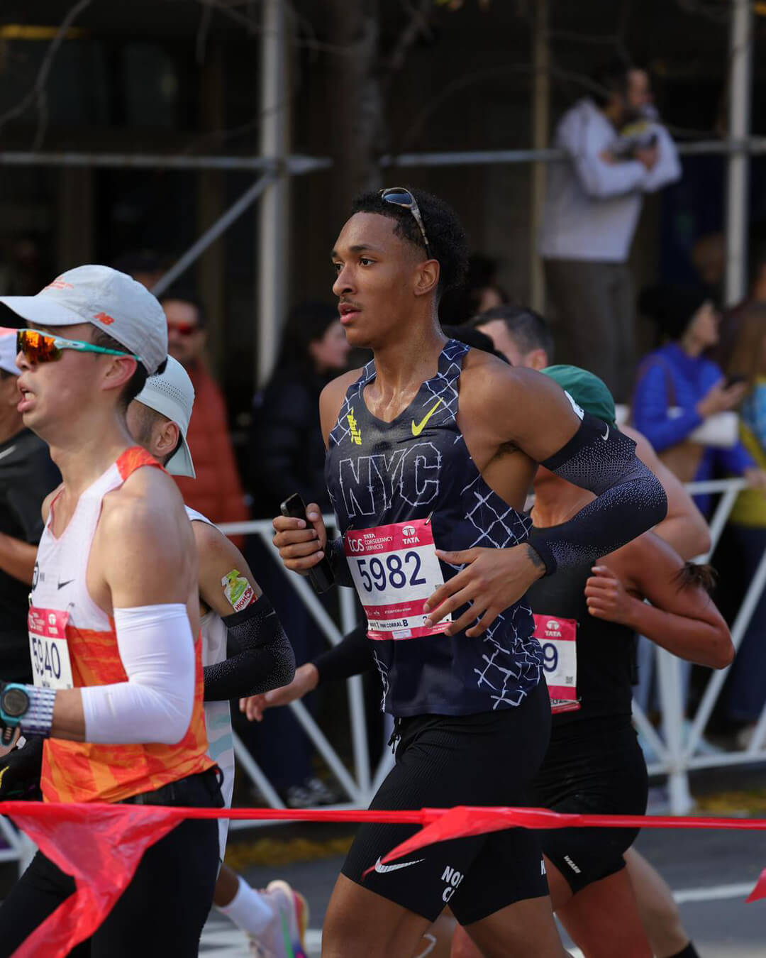 Male runners competing in a marathon, one wearing an NYC tank top and bib number 5982.