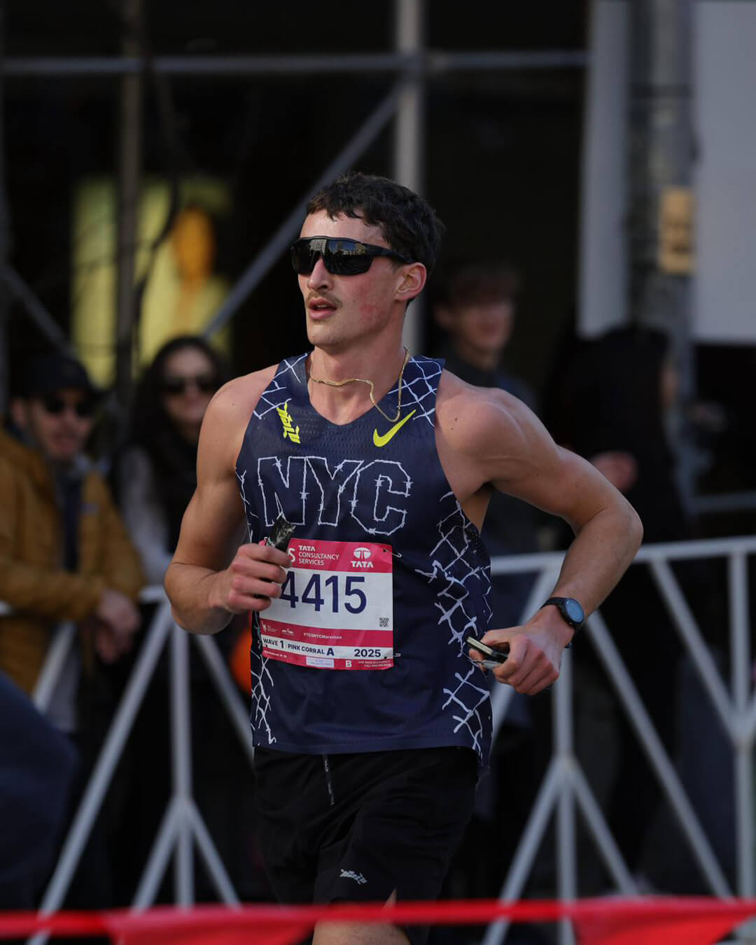 Male runner wearing dark sunglasses and a sleeveless NYC race shirt with bib number 4415 during a marathon.