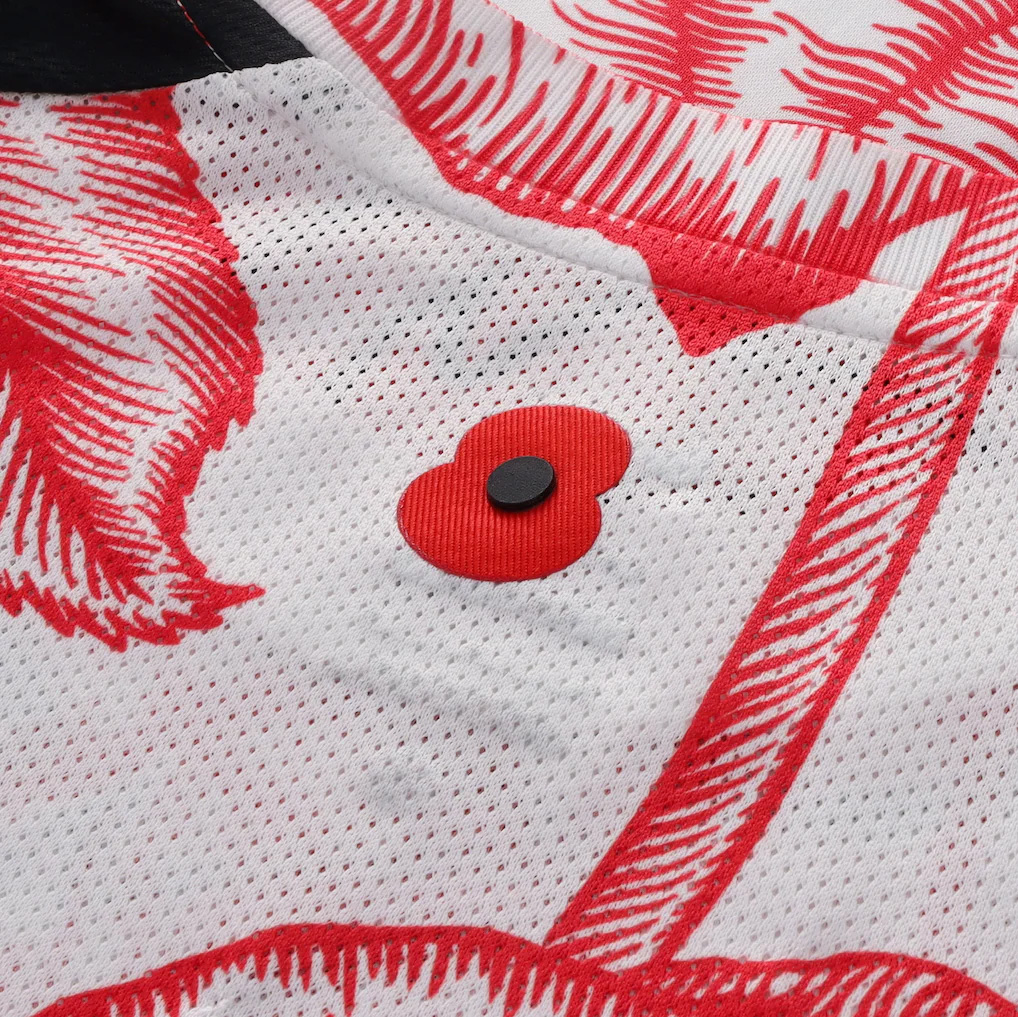 Close-up of a white sports jersey with red printed details and a red poppy flower emblem with a black center.