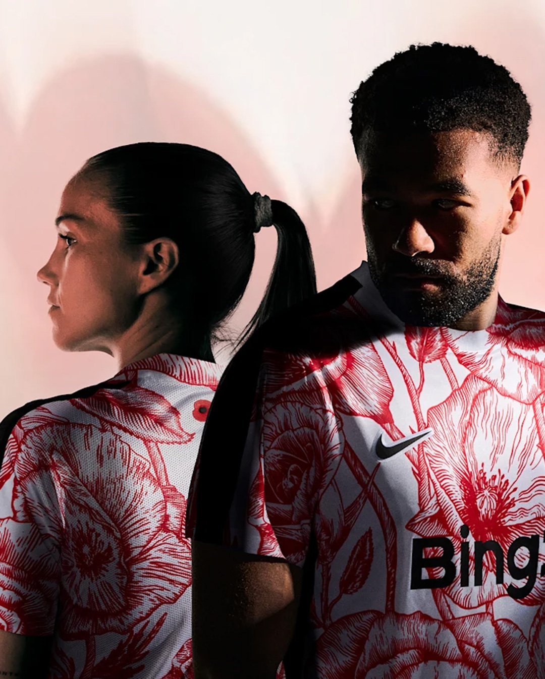A man and woman standing back to back wearing white sports jerseys with red floral patterns and black accents.