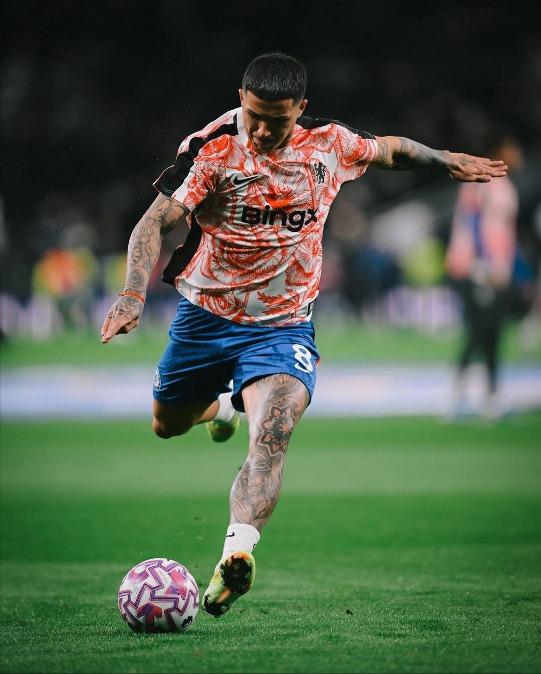 Soccer player wearing a floral patterned jersey and blue shorts kicking a pink and white ball on the field.