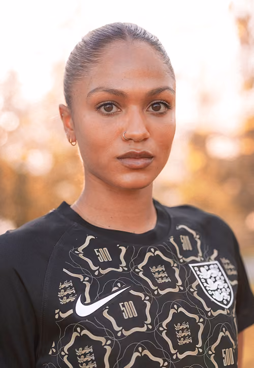 Close-up of a woman with a nose ring wearing a patterned England soccer jersey with Nike logo outdoors.