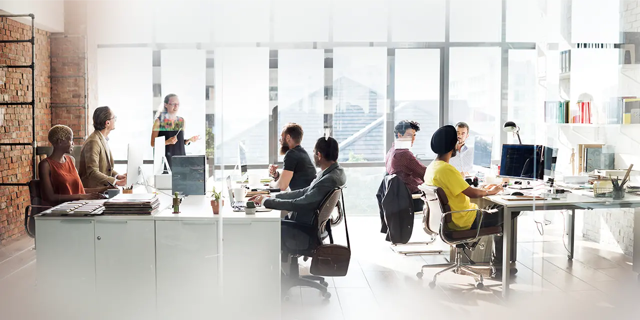 A group of people sitting in an office with a woman standing in front of them.