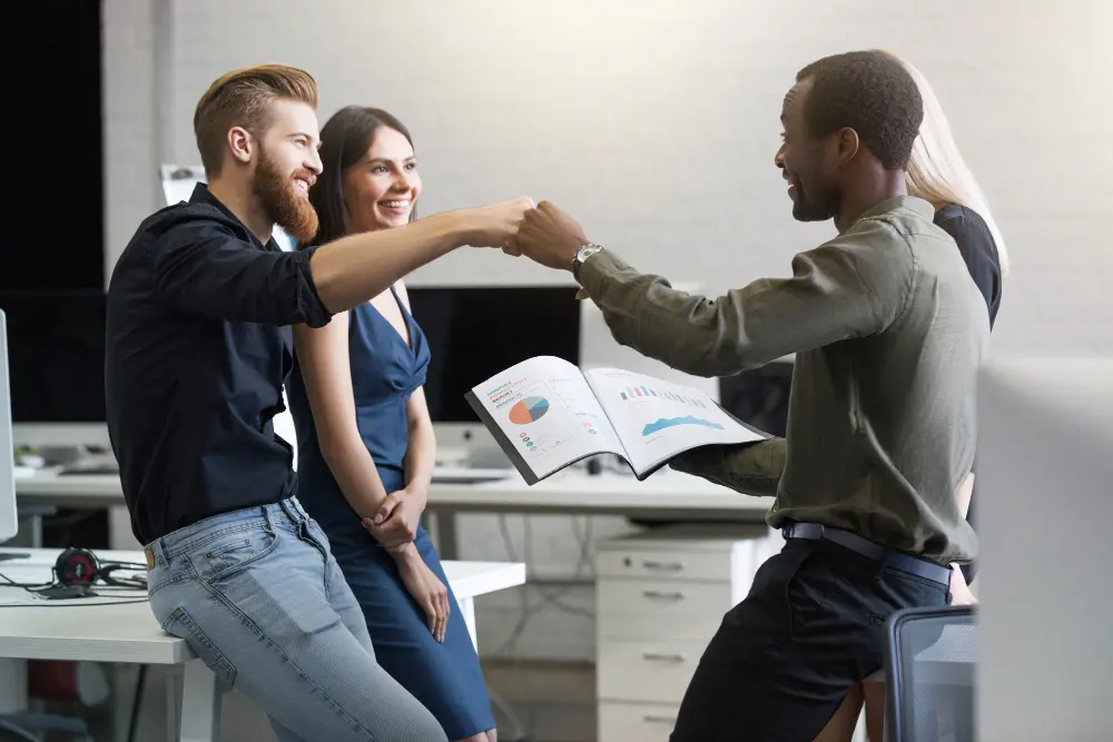 Coworkers celebrating with a fist bump in an office.