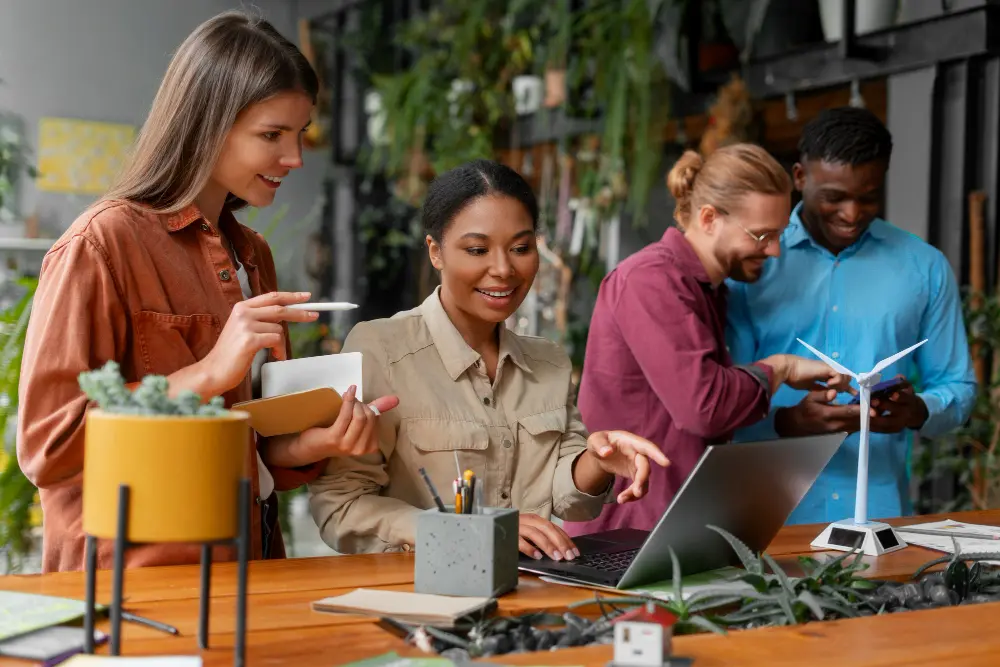 Four people in a collaborative work environment, interacting with a laptop, notes and a model wind turbine.