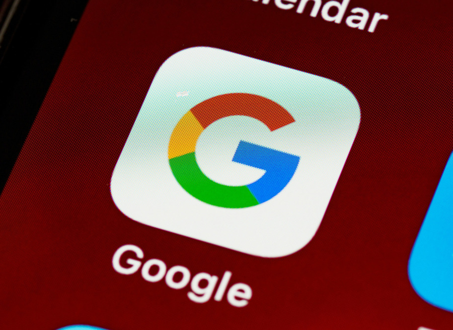 Google app icon with multicolor ‘G’ logo displayed on a smartphone screen against a red background. 
