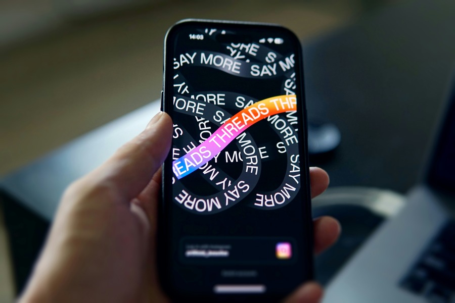 Person holding a smartphone displaying the Threads app login screen with vibrant "Say More" graphics and Instagram logo.