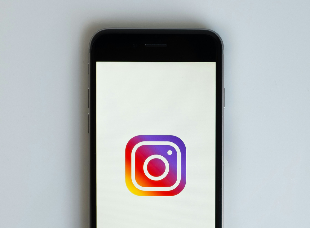 Smartphone displaying the Instagram app logo with vibrant colors—purple, red, yellow—on a light background.
