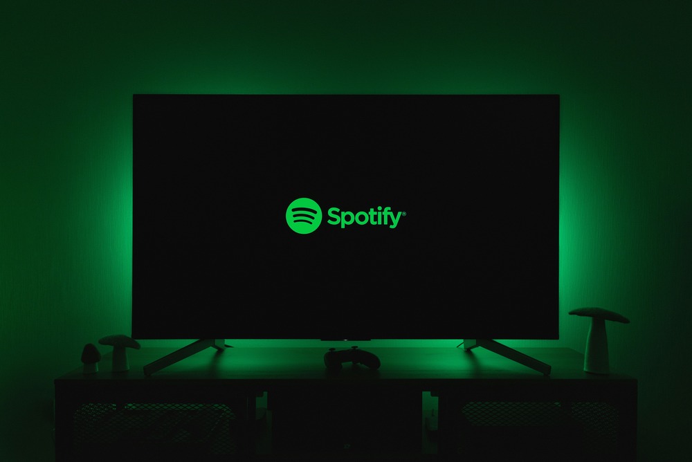Spotify logo in bright green on a large TV screen with matching green ambient lighting in a dark entertainment setup.