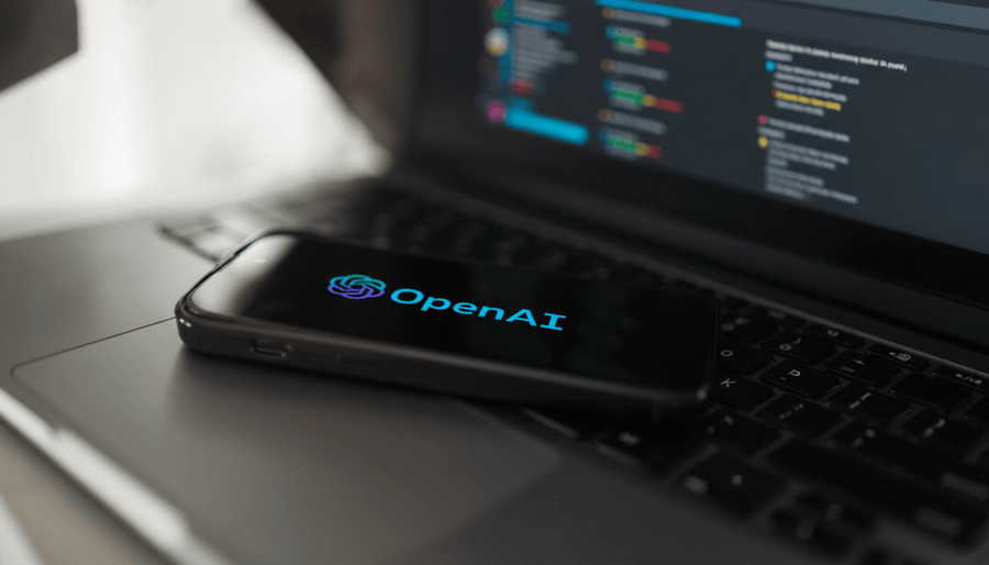 OpenAI logo glowing in blue-purple on smartphone screen placed on laptop keyboard with code editor in background.