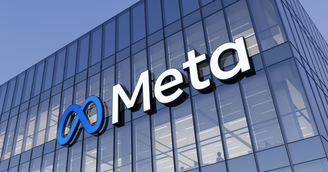 Meta logo on modern glass building facade, featuring blue infinity symbol and white "Meta" text against clear blue sky.