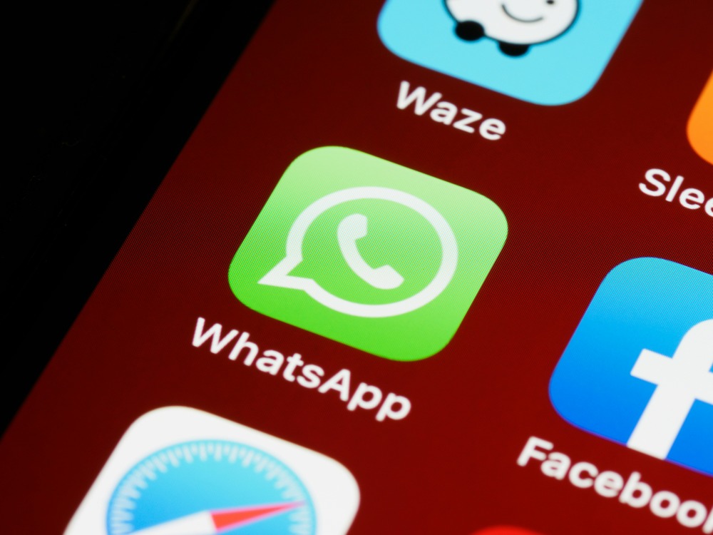 WhatsApp green speech bubble logo icon on smartphone home screen close-up, surrounded by Waze, Sleeper, Facebook, and other app icons.