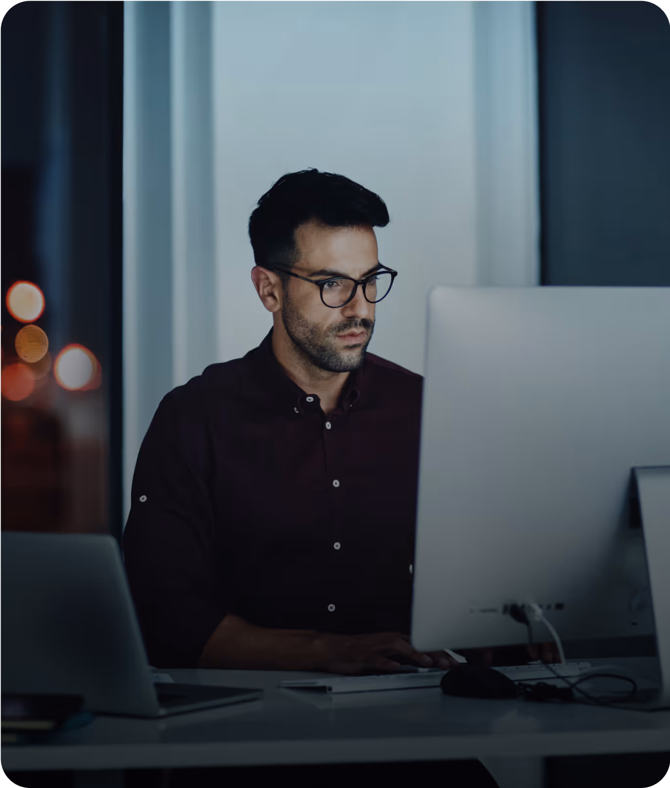 A man wearing glasses is focused on working at a computer in an office.