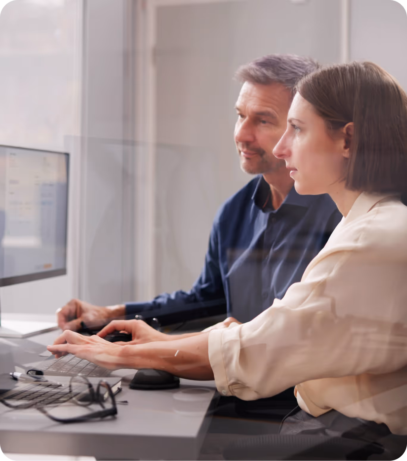 Two people focused on a computer screen while working together in an office setting.