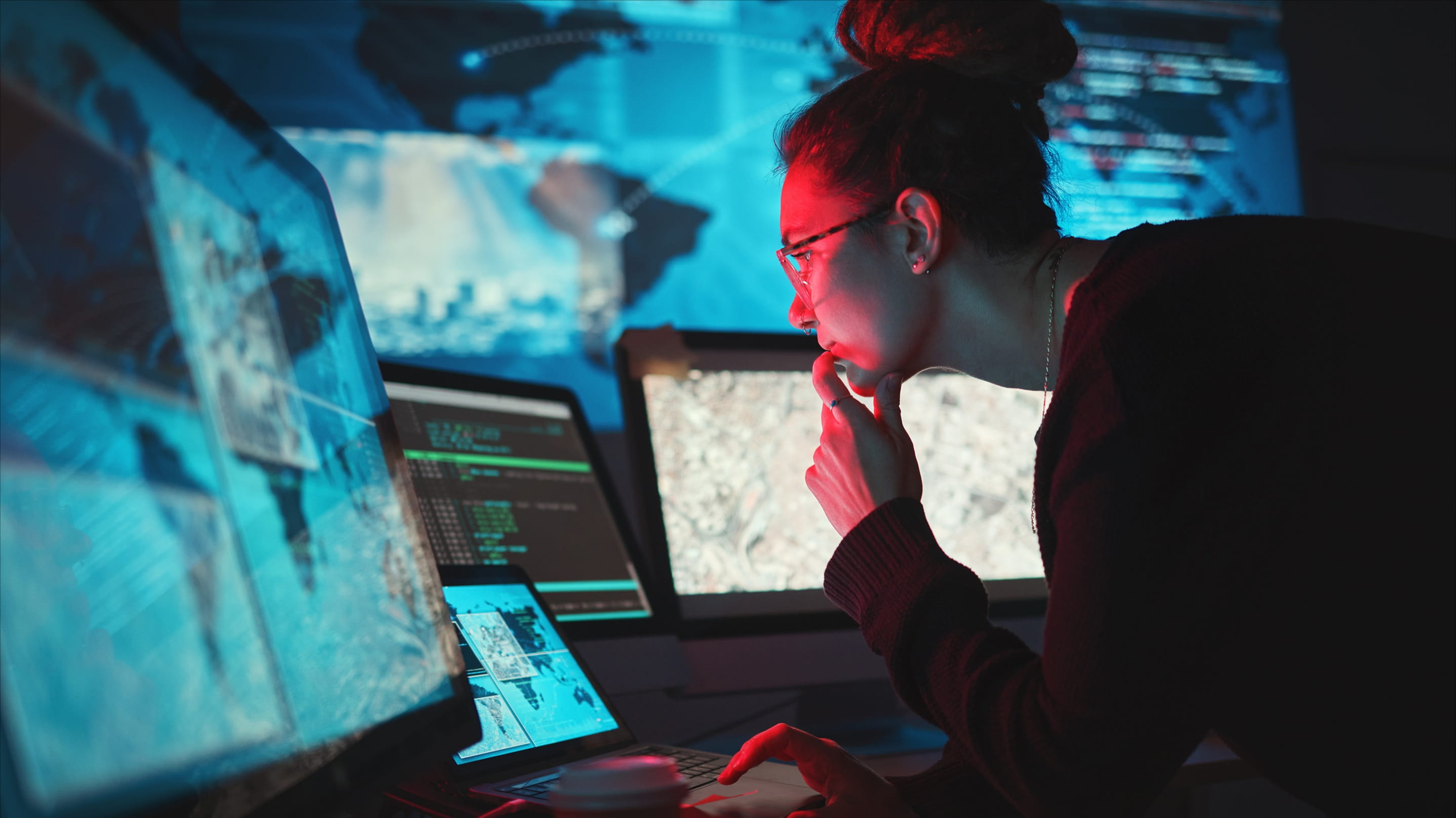 A cybersecurity analyst monitors multiple screens displaying code and global threat data in a darkened operations centre