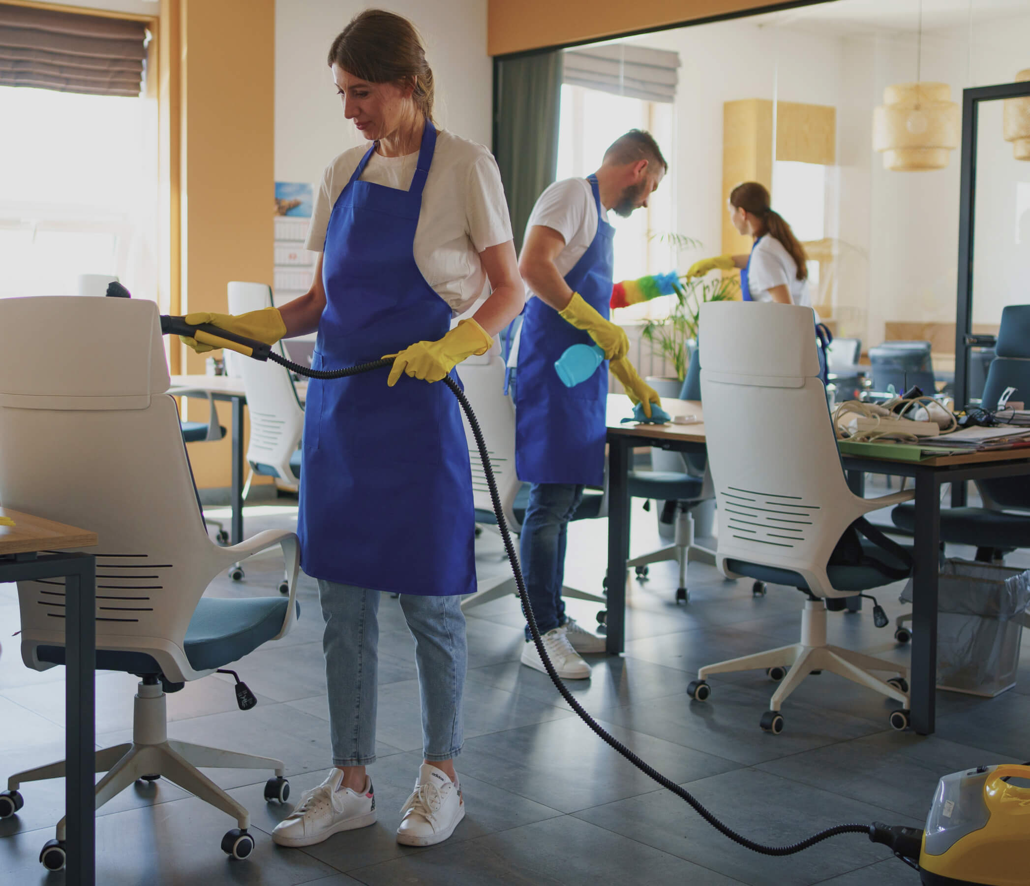 A woman in an office cleaning the floor with a vacuum.