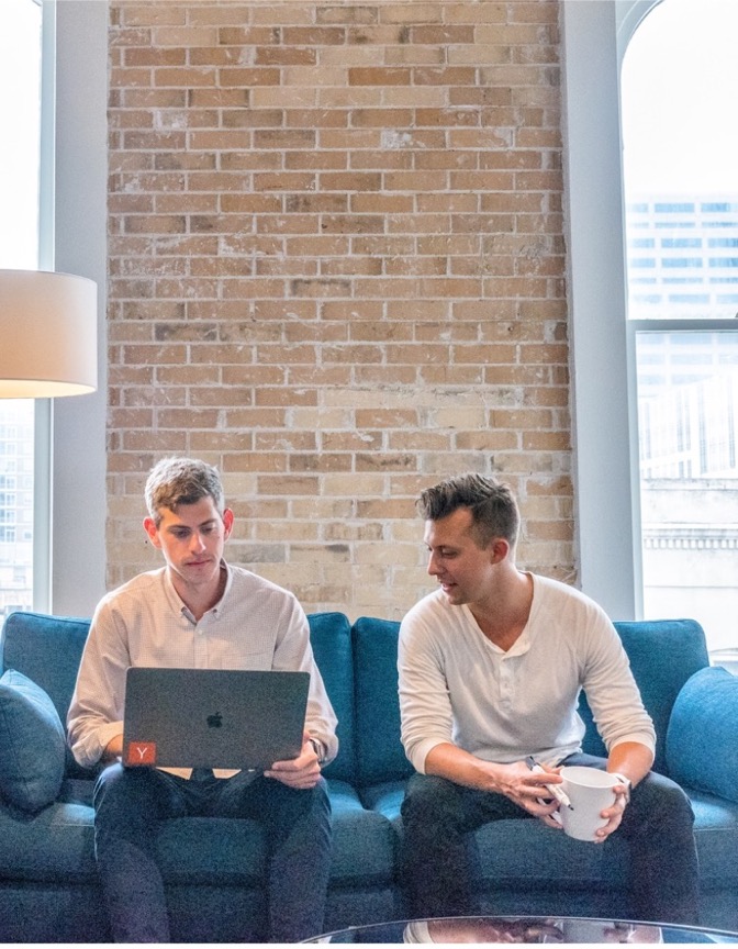 Two people sit on a couch looking an opened laptop
