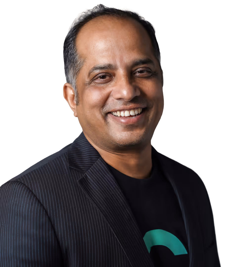 Smiling man wearing a dark patterned blazer and black t-shirt with a green design on a white background.