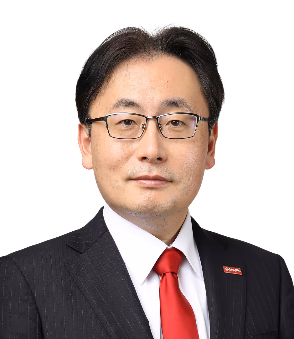 Man with black hair wearing glasses, a black pinstripe suit, white shirt, and red tie with MUFG lapel pin.