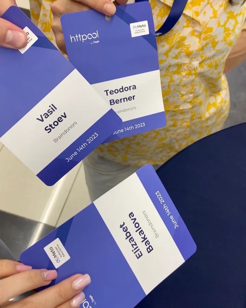 Three hands holding blue and white event badges with names Vasil Stoev, Teodora Berner, and Elizabet Bakalova, dated June 14th 2023.