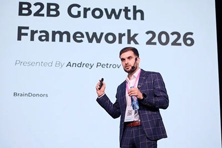 Presenter Andrey Petrov wearing suit speaking with headset microphone on B2B Growth Framework 2026 stage.