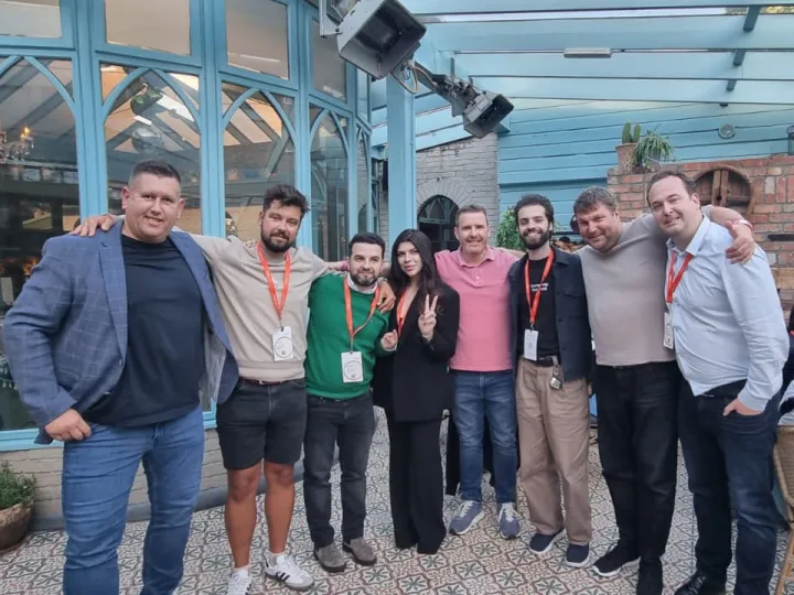 Group of eight people standing together outdoors with arms around each other, smiling at the camera.